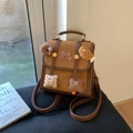 Detail van de bruine patchwork rugzak met pluche hangers en strikdecoratie op de flap - Bruin