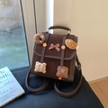 Detail van bruine suède rugzak met schattige pluche patches en een rode strik - Bruin