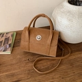 Detail of tan matte leather crossbody bag featuring a silver twist lock and wooden background - Brown