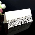 White laser cut wedding place card with intricate leaf patterns on a black background - White