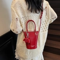 Glossy red bucket bag with elephant charm and shoulder strap on a model - Burgundy