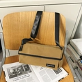 Khaki canvas cylinder shoulder bag with black strap and zipper in a lifestyle setting - Khaki