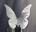 Close-up of laser-cut silver butterfly place card with rose hollow design on glass rim - Reflective Silver