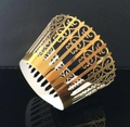 Macro shot of gold laser-cut lace cupcake liners with floral pattern on black surface - Reflective Gold