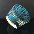Detail of laser-cut lake blue cupcake wrapper with decorative floral vine patterns - Reflective Blue