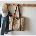 Detalle del bolso tote de lona con correas marrones y etiqueta de cuero en gancho de madera - Caqui