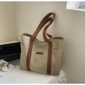Dettaglio borsa tote in tela kaki con manici marroni e tasche laterali sulla scrivania - Cachi