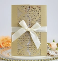 Nahaufnahme der goldfarbenen, lasergeschnittenen Hochzeitseinladung mit Seidenschleife - Beige Gold