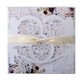Detail view of laser-cut wedding invitation with silk ribbon bow and floral pattern - White