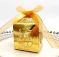 Close-up of golden laser-cut Ganesha candy box with orange ribbon on white porcelain - Reflective Gold