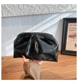 Detail of a black glossy pleated clutch bag on a wooden table with a minimalist background - Black