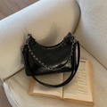 Bolso medialuna negro brillante con cadena plateada y logo sobre un sofá beige - Negro Grande