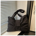 Detail of black bow-shaped nylon shoulder bag with wide strap by a minimalist window - Black