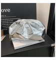 Detail of silver metallic dumpling clutch bag with chic pleats on top of books - Silver