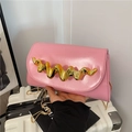 Sac bandoulière en cuir verni rose avec barre dorée ondulée et chaîne sur une valise - Rose