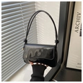 Detail of glossy black patent leather bag featuring wavy flap and knotted shoulder strap - Black