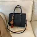 Black textured tote bag with pompom charm and shoulder strap on beige background - With Charm / Black
