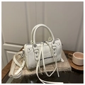 Détail du sac Boston blanc cassé avec rivets et longs pompons sur fond en tricot - Blanc