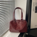 Minimalist burgundy high-gloss leather satchel handbag with dual handles on a windowsill - Red