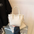 Sac seau beige minimaliste à bord ondulé posé sur une valise argentée et un livre - Sans Pendentif / Blanc