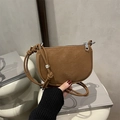 Bolso bandolera de cuero marrón con forma de media luna y letras doradas en estudio zen - Marrón