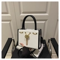 Moderne weiße Lederhandtasche mit schwarzen Akzenten und goldener Kette auf Sitz - Weiß