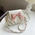 Cream pleated shoulder bag with pink bow accent and braided rope strap on table - White
