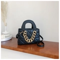 Close-up of black quilted crossbody bag with bold gold chain on a wooden shelf - Black