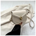 Close-up of cream saddle bag featuring a signature gold circular buckle and metal hardware - White