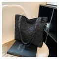 Bolso tote acolchado negro con diseño de diamantes y correas largas sobre una silla - Negro