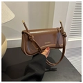 Close-up of brown leather underarm bag featuring decorative knots and gold logo - Dark Brown