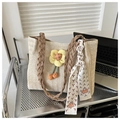 Close-up of beige straw tote bag featuring yellow flower charm and patterned silk scarf - Khaki