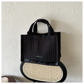 Bolso tote acolchado negro con costuras verticales y etiqueta de moda en silla de mimbre - Negro