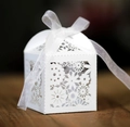 Laser-cut white wedding favor box with floral patterns and ribbon on dark wood background - White