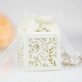 Close-up of laser-cut cream wedding favor box with intricate lace floral and white ribbon - Ivory