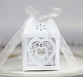 Macro shot of white laser-cut wedding favor box with heart patterns and silk ribbon bow - White