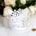 Detail of white laser-cut cupcake wrappers with intricate snowflake patterns for holidays - White
