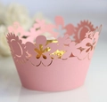 Close-up of laser-cut pink paper cupcake wrapper with floral hollow patterns - Pink