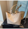 Primer plano de bolso tote trenzado beige con textura fina y detalles de remaches dorados - Caqui
