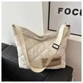 Detail der cremefarbenen Stepptasche mit braunem Lederpatch auf schwarzem Ledersofa - Weiß