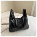 Detail of black glossy PU leather hobo bag with silver buckle on a textured surface - Black