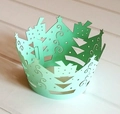 Laser-cut Christmas tree cupcake liners in light green on a white wooden background - Fruit Green