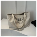 Detail view of cream tote bag featuring silver chain, bow buckle and metallic charms - Off White