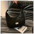 Close-up of black nylon crescent bag with branded label on grey suit fabric background - Black