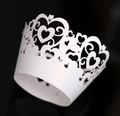 Detailed laser-cut heart lace pattern on a white paper cupcake wrapper over black background - White