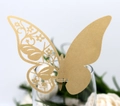 Close-up of golden laser-cut butterfly place card with intricate floral hollow pattern - Beige Gold