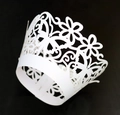 Macro detail of laser-cut white cupcake liners with hollow floral and butterfly patterns - White
