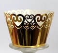 Detailed macro of golden laser-cut cupcake wrapper with heart pattern on glass stand - Reflective Gold