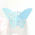Détail macro du marque-place papillon ajouré bleu clair posé sur un bord de verre - Bleu Pâle Perlé