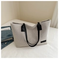 Detail shot of woven canvas tote bag featuring black leather logo and shoulder straps - Black